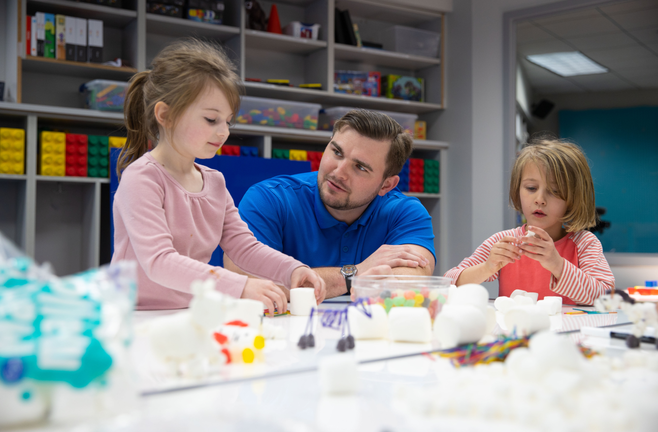 A man is helping two little girls with arts and crafts.