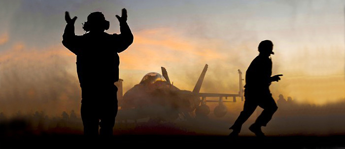 Crew members on an aircraft carrier direct an FA-18 jet.